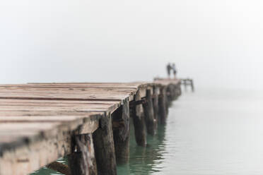 Unrecognizable blurred couple standing on wooden quay in sea water in foggy morning on Playa de Muro - ADSF29479