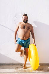 Mann ohne Hemd mit aufblasbarem Ring an der Wand lehnend an einem sonnigen Tag - OCMF02213