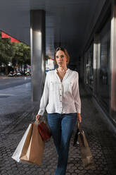 Selbstbewusste junge Frau mit Einkaufstüten auf dem Fußweg - JRVF01727