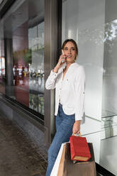 Junge Frau mit Einkaufstüten, die mit einem Mobiltelefon telefoniert - JRVF01730