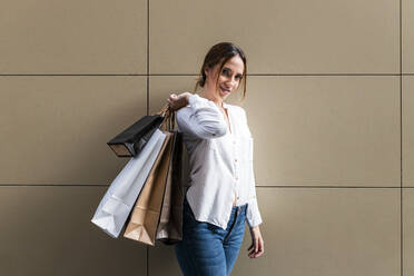 Junge Frau trägt Einkaufstaschen, während sie in der Nähe der Wand steht - JRVF01739