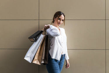 Young woman carrying shopping bags while standing near wall - JRVF01739