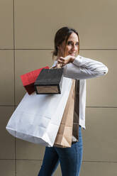 Smiling young woman with shopping bags in front of wall - JRVF01740