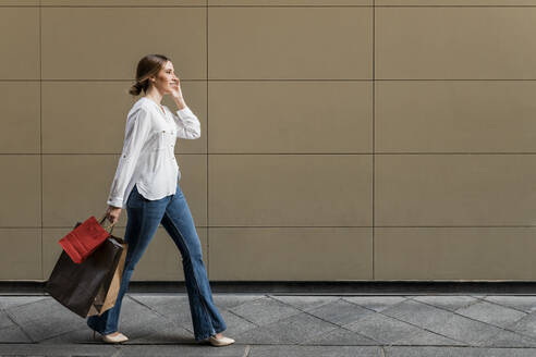 Frau schaut weg, während sie mit Einkaufstüten auf dem Gehweg geht - JRVF01741