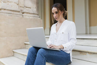 Freiberuflerin mit Laptop im Sitzen auf der Treppe - JRVF01747