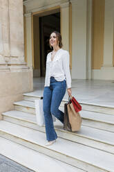 Lächelnde Frau mit Einkaufstaschen auf der Treppe - JRVF01750