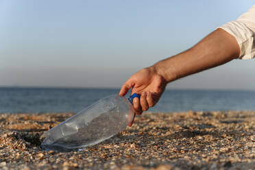 Man picking plastic bottle on sand at beach - EYAF01728