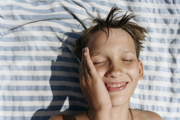 Lächelnder Junge mit geschlossenen Augen auf einem Handtuch liegend - EYAF01731