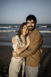 Smiling young couple embracing each other on beach - RCPF01209