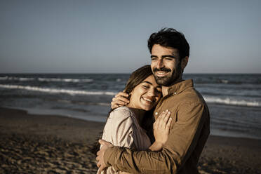 Glückliches junges Paar, das sich am Strand umarmt - RCPF01213