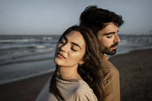 Couple with eyes closed leaning on each other at beach - RCPF01219