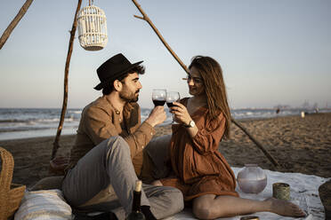 Paar stößt auf ein Getränk an, während es auf einer Picknick-Decke sitzt - RCPF01229