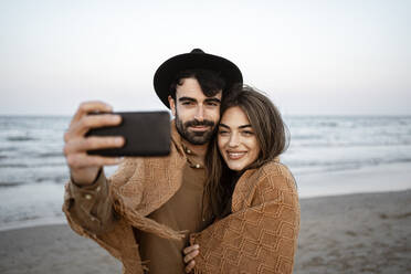 Freund nimmt Selfie mit Freundin durch Mobiltelefon am Strand - RCPF01244