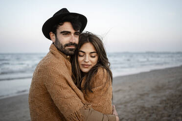 Young couple embracing while standing at beach during sunset - RCPF01245