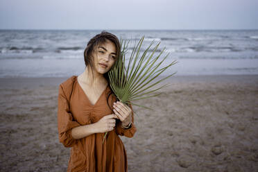 Thoughtful woman holding leaf while standing at beach - RCPF01251