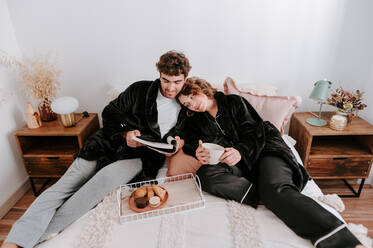 High angle of gentle couple relaxing on bed together while having breakfast in morning - ADSF29501