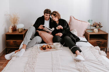 High angle of gentle couple relaxing on bed together while having breakfast in morning - ADSF29504