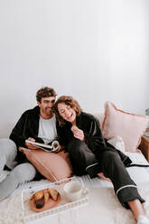 High angle of gentle couple relaxing on bed together while having breakfast in morning - ADSF29505