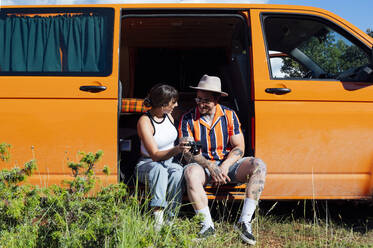 Ein reiselustiges Paar sitzt im Van und schaut sich die Fotos auf der Kamera während eines Sommerabenteuers an - ADSF29511