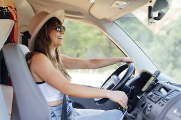 Seitenansicht einer lächelnden weiblichen Reisenden, die auf dem Fahrersitz eines Lieferwagens sitzt und einen Roadtrip im Sommer genießt - ADSF29514