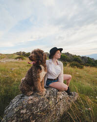Besitzerin mit gehorsamem Labradoodle-Hund sitzt auf einem Felsen in den Bergen - ADSF29538