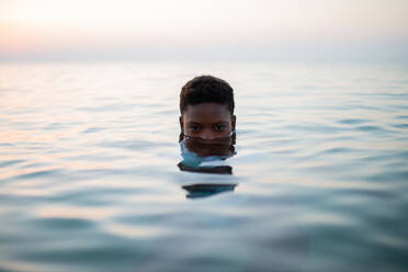 Afroamerikanische Frau mit halbem Gesicht im Meerwasser schaut in die Kamera vor dem Hintergrund des Sonnenuntergangs - ADSF29549