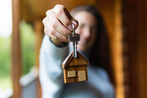 Unscharfe anonyme Eigentümerin zeigt die Schlüssel des neuen Hauses, während sie auf einer Holzterrasse in den Pyrenäen steht - ADSF29606