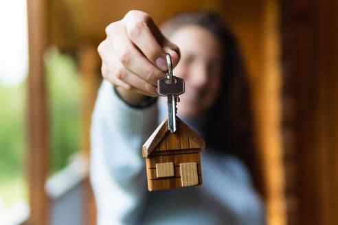 Blurred anonymous female owner showing keys of new house while standing on wooden terrace in Pyrenees - ADSF29606