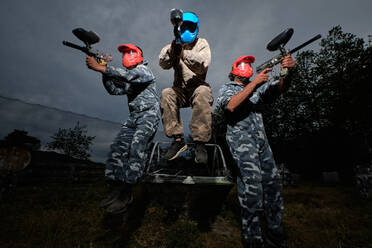 Niedriger Winkel von Teams von Paintball-Spielern in Tarnkleidung und mit Gewehren auf dem Hintergrund des bewölkten Himmels am Abend - ADSF29639