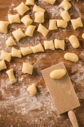 Top view of pieces of soft raw dough placed on wooden table covered with flour near ribber board during gnocchi preparation in the kitchen - ADSF29652