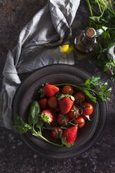 Draufsicht auf eine Schüssel mit frischen Erdbeeren und Tomaten zur Zubereitung einer kalten Gazpacho-Suppe auf einem dunklen Tisch - ADSF29671