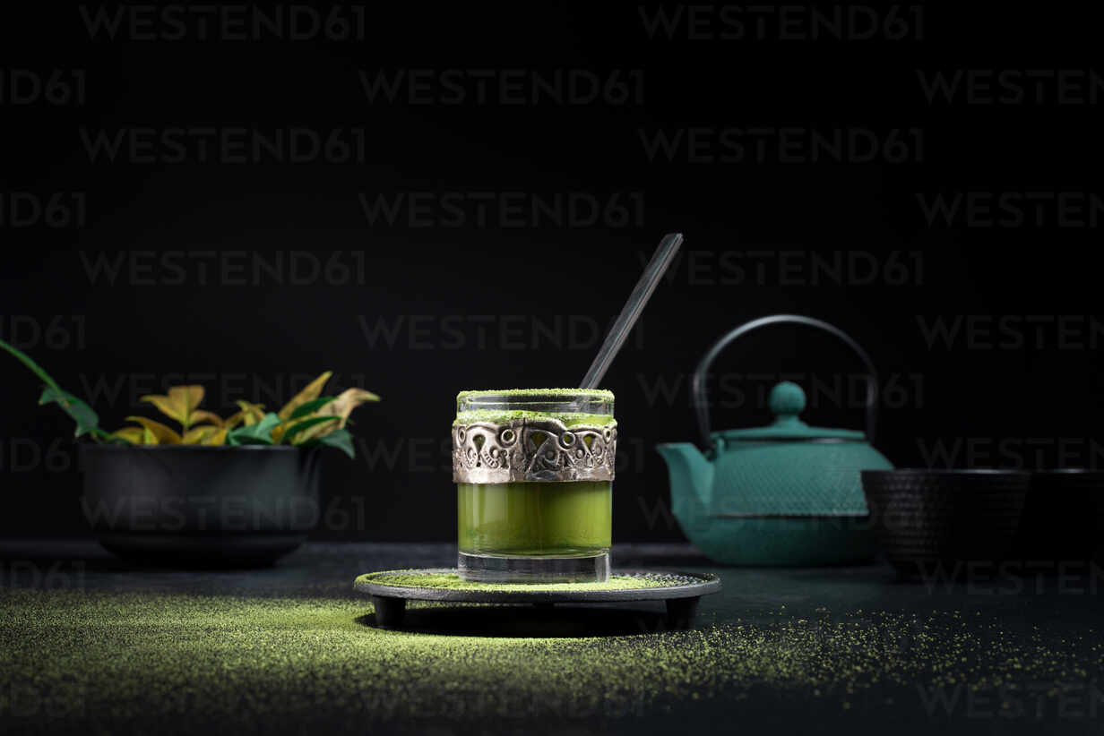 https://us.images.westend61.de/0001602196pw/still-life-composition-with-traditional-oriental-matcha-tea-served-in-glass-cup-with-metal-ornamental-decor-on-table-with-ceramic-bowls-and-fresh-green-leaves-against-black-background-ADSF29675.jpg