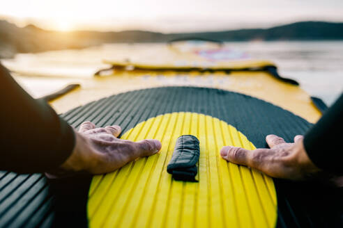 POV Ansicht der Ernte Hände von anonymen männlichen Surfer schwimmen auf SUP-Board im Meer bei Sonnenuntergang - ADSF29692