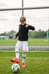 Begeisterter Jugendlicher in Sportkleidung mit Ball auf einem Fußballplatz in der Nähe des Netzes - ADSF29696