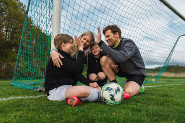 Eine Familie in Sportkleidung, die sich am Wochenende auf einem grünen Fußballplatz versammelt, um sich zu begrüßen - ADSF29697