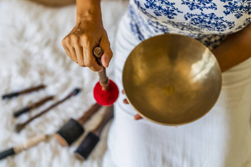 Female sound therapist playing brass bowl with mallet in studio - DLTSF02136