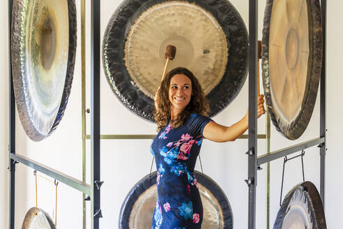 Female professional therapist playing gongs with mallets in studio - DLTSF02138