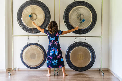 Female sound therapist playing gongs with mallets in studio - DLTSF02140