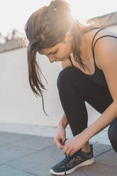 Young woman tying shoelace while crouching on footpath - AFVF09136