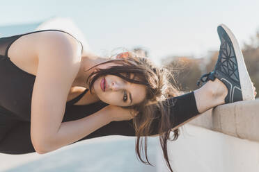 Woman stretching leg while leaning on retaining wall - AFVF09137