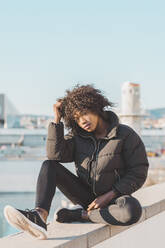 Afro-Frau mit Hand im Haar auf Stützmauer sitzend - AFVF09138