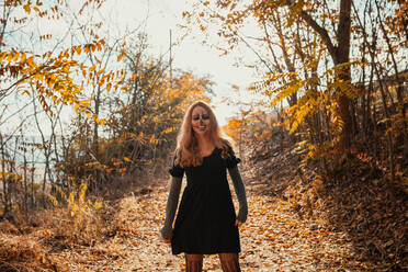 Smiling woman with Halloween make-up standing in forest during autumn - MRRF01461