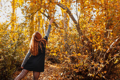 Woman stretching hand while standing in forest during autumn - MRRF01485