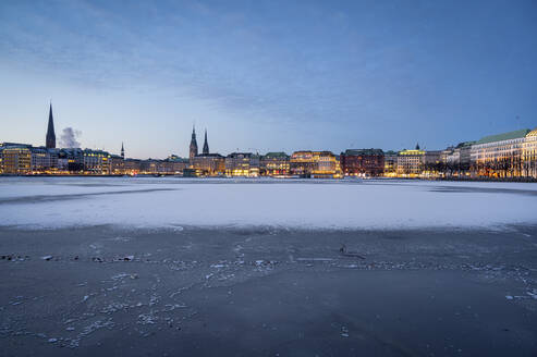 Deutschland, Hamburg, Gefrorene Oberfläche der Binnenalster in der Morgendämmerung mit Stadtsilhouette im Hintergrund - RJF00873