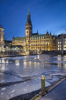 Deutschland, Hamburg, Eis schwimmend im Stadtkanal in der Abenddämmerung mit Hamburger Rathaus im Hintergrund - RJF00876