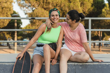 Frau sitzt mit Arm um Freundin im Skateboardpark - JRVF01761