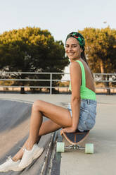 Mittlere erwachsene Frau auf Skateboard sitzend - JRVF01765