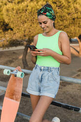 Frau benutzt Mobiltelefon, während sie sich auf ein Geländer stützt - JRVF01766