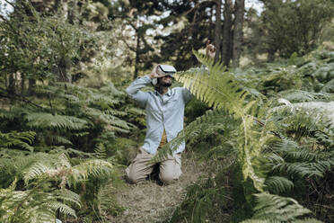 Mann benutzt ein Virtual-Reality-Headset, während er im Wald kniet - JCCMF03788