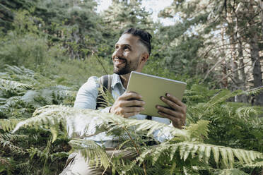 Lächelnder männlicher Hipster mit digitalem Tablet im Wald - JCCMF03796